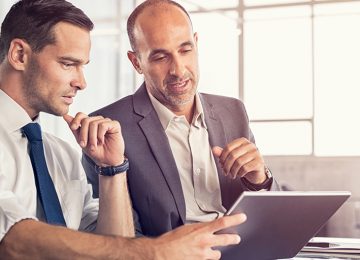 Image of two men in office looking at tablet and discussing business tax reform