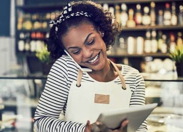 Image of young business owner talking on phone and looking at tablet - holiday giving