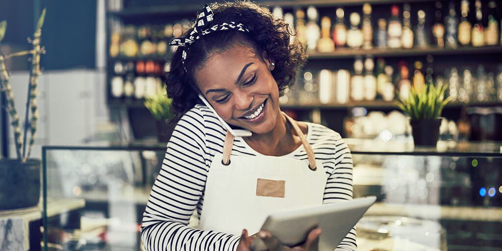 Image of young business owner talking on phone and looking at tablet - holiday giving