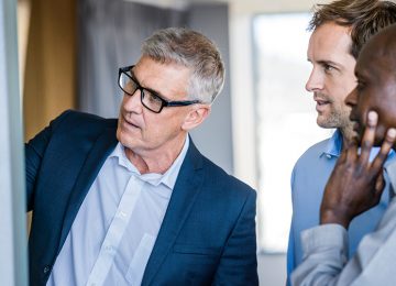 Image of three business men looking at whiteboard as one man outlines benefits of structuring business as a corporation