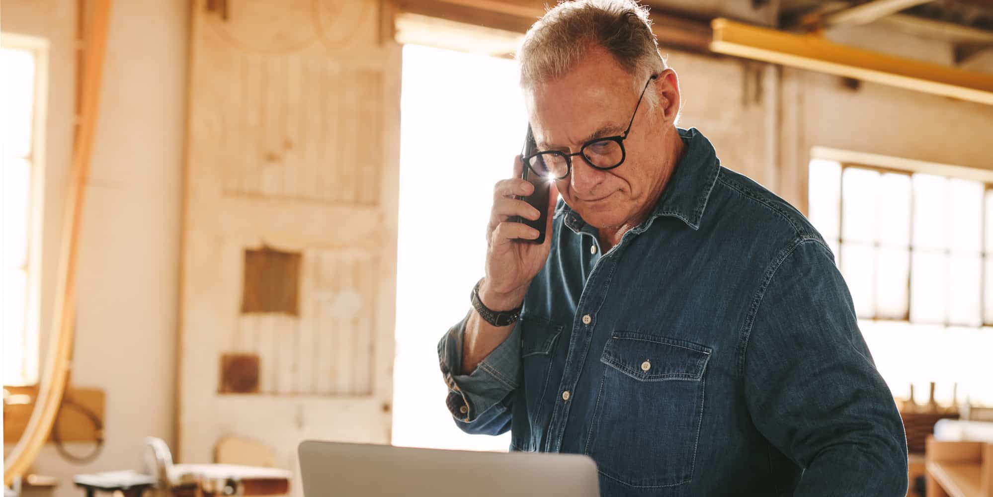 Senior male carpenter standing in workshop is targeted in social security number phone scam