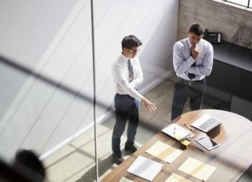 Two businessmen standing in office and talking about business losses affecting QBI deduction