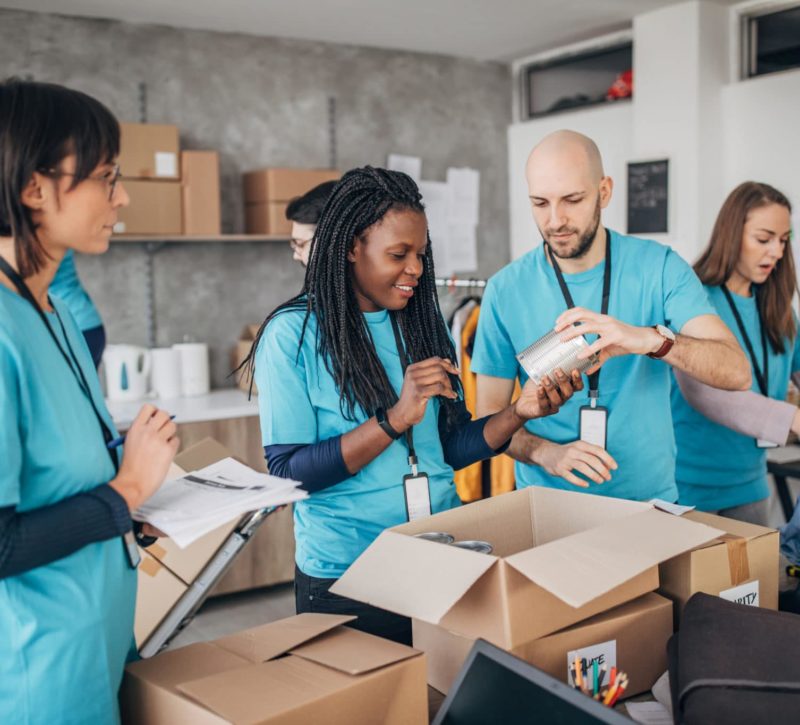 Multi-ethnic group of people, diverse volunteers packing donation boxes in charity food bank.