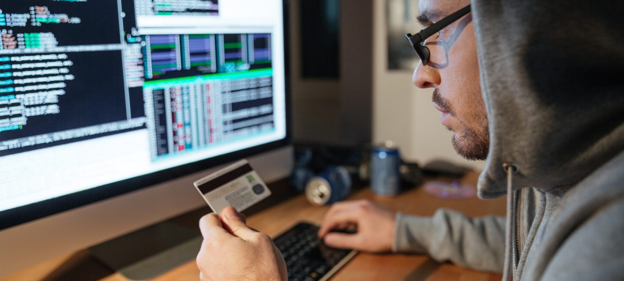 Image of young hacker at computer and using credit card for identity theft