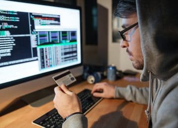 Image of young hacker at computer and using credit card for identity theft