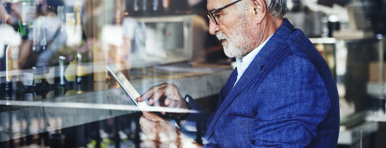 Image of older gentleman looking at tablet in bar and thinking about his succession plan