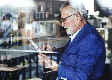 Image of older gentleman looking at tablet in bar and thinking about his succession plan