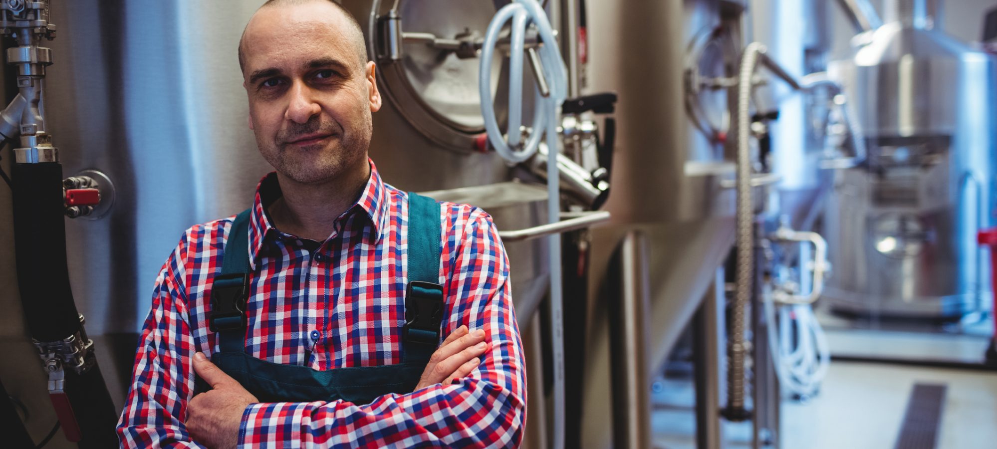 Image of man with arms crossed standing by storage tanks at brewery - retained earnings