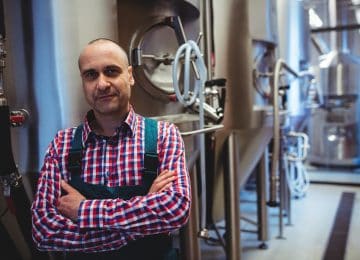 Image of man with arms crossed standing by storage tanks at brewery - retained earnings