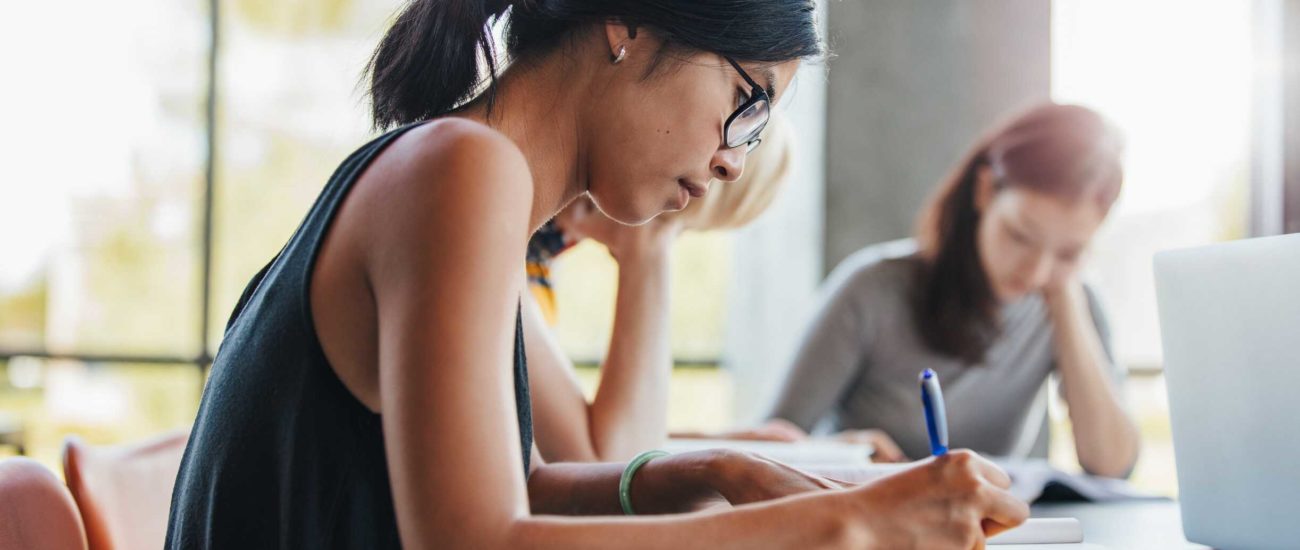 Close-up image of young woman studying at library and writing notes about tax credits for college students