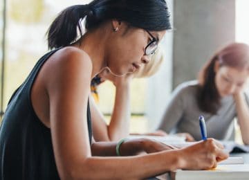 Close-up image of young woman studying at library and writing notes about tax credits for college students