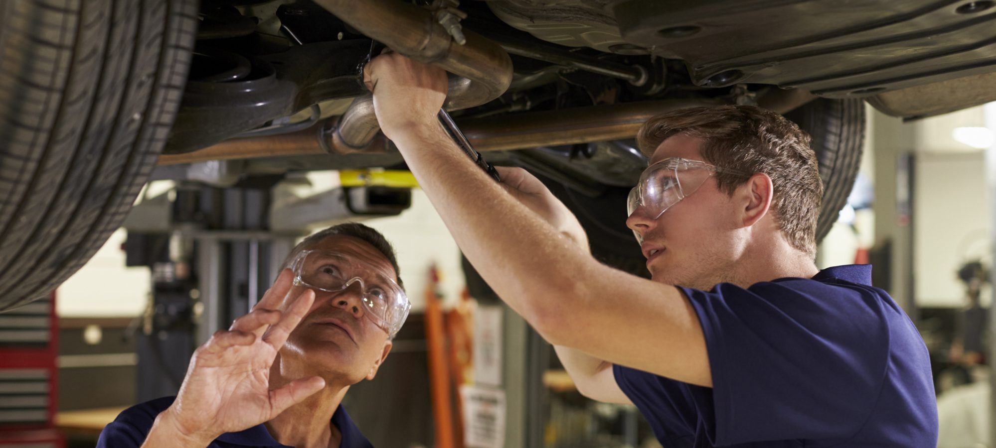 Image of mechanic and son working underneath car together - hiring your child in your business