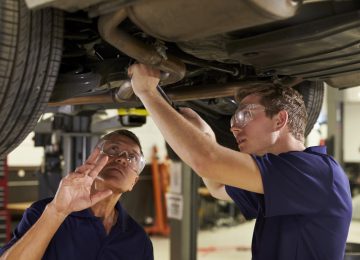 Image of mechanic and son working underneath car together - hiring your child in your business