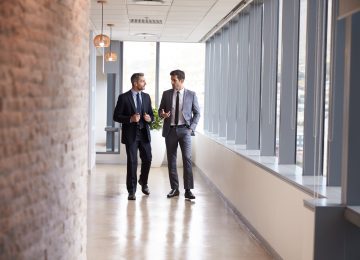 Image of two businessmen having informal meeting about qualified business income deduction in office corridor