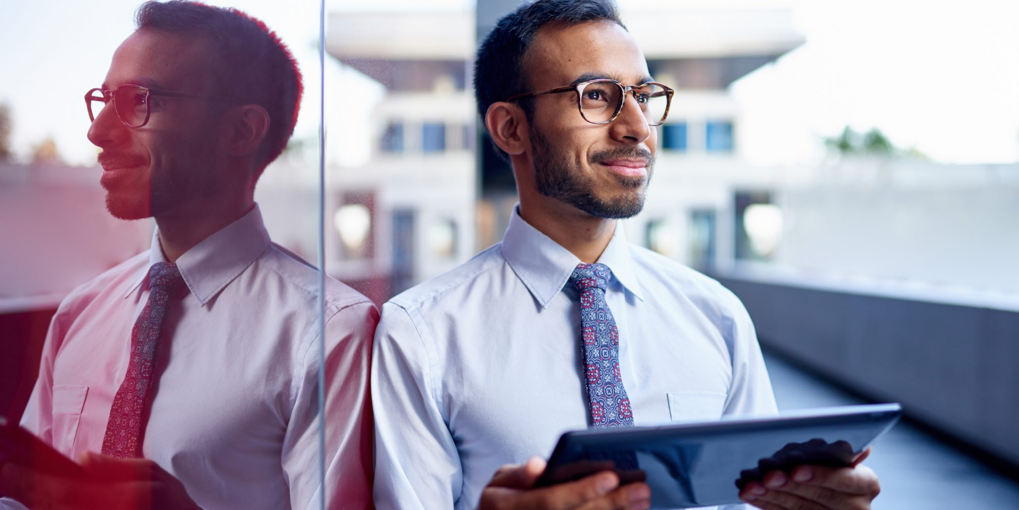 Image of young businessman leaning against wall with tablet - should he buy a business?