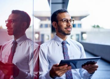 Image of young businessman leaning against wall with tablet - should he buy a business?