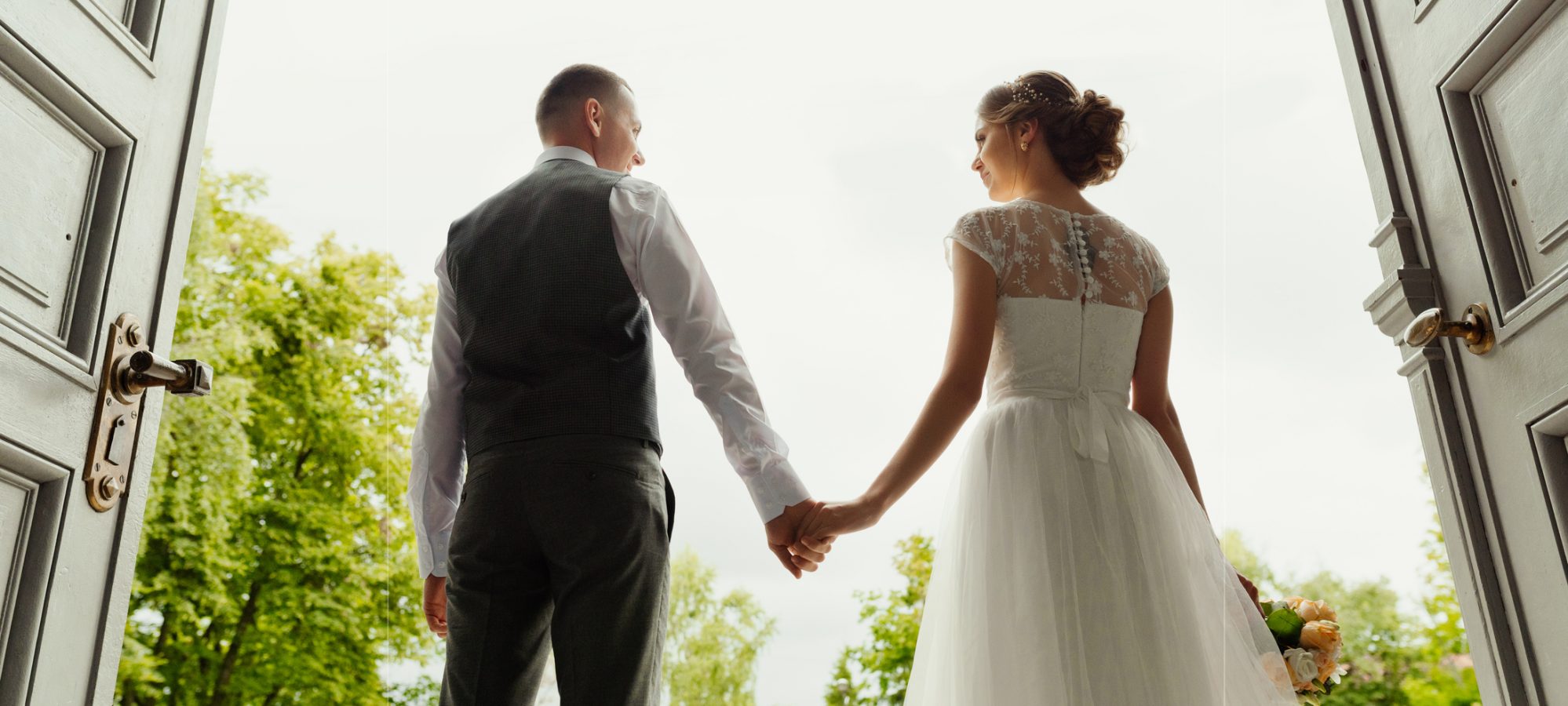 Image of bride and groom - newlyweds - standing against the background of cathedral exit and holding hands