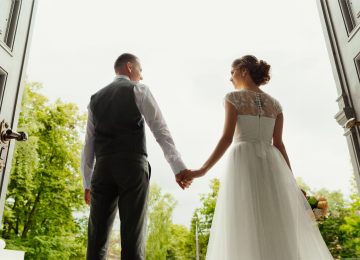 Image of bride and groom - newlyweds - standing against the background of cathedral exit and holding hands