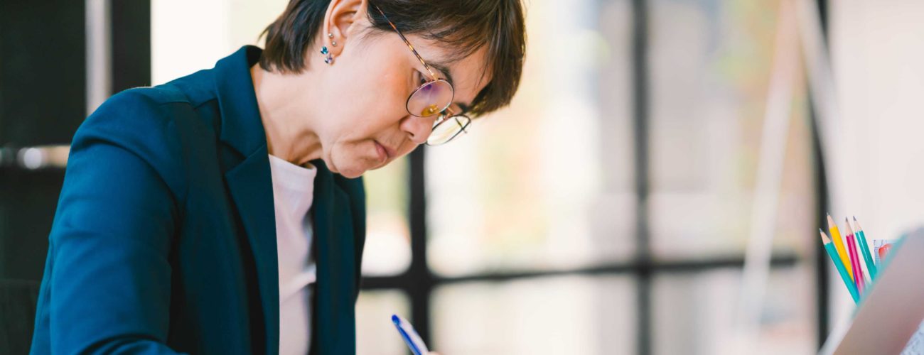 Image of middle age woman sitting at desk in office and calculating her 2018 QBI deduction