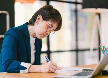 Image of middle age woman sitting at desk in office and calculating her 2018 QBI deduction