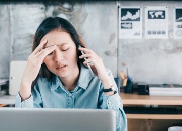 Image of young business woman who's on phone with current payroll provider and stressed