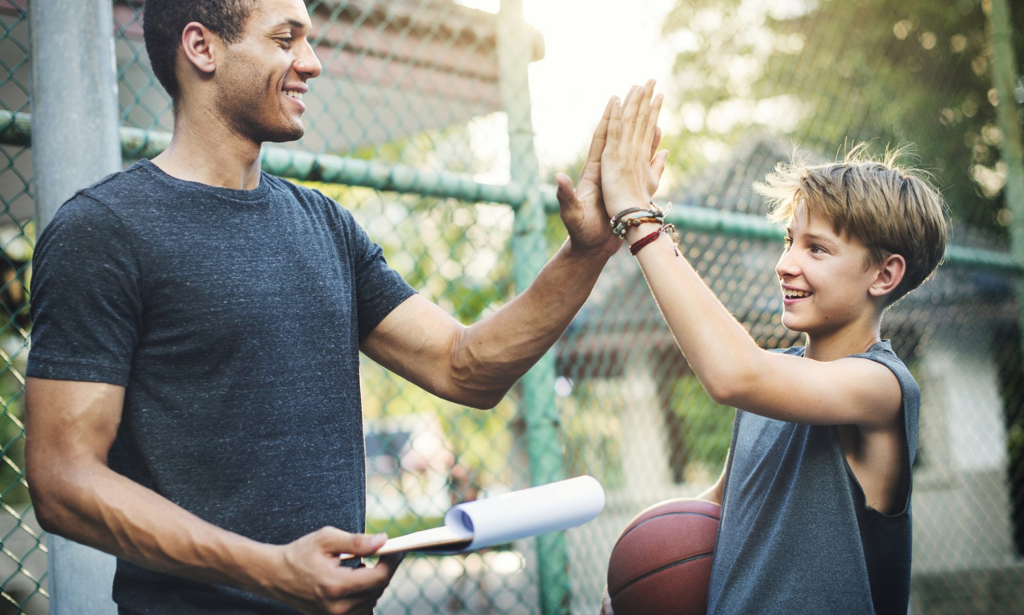 Image of young boy and volunteer coach high fiving after basketball practice