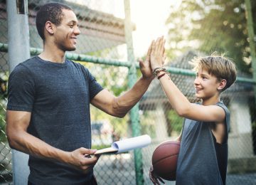 Image of young boy and volunteer coach high fiving after basketball practice