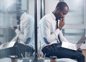 Image of business man sitting on desk and carefully reviewing a phishing attempt on his laptop