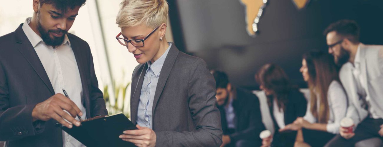 Image of man and woman reviewing retirement plans with business team working in background