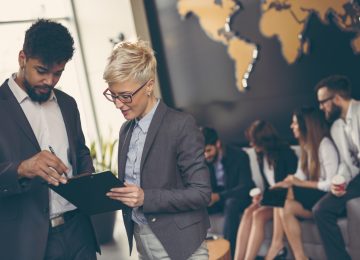 Image of man and woman reviewing retirement plans with business team working in background