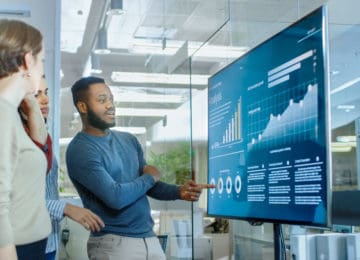 Four coworkers looking at company's real-time financial data on digital screen