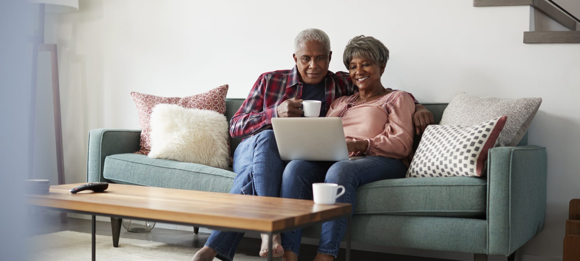 Image of married couple sitting on couch and checking status of tax refund on laptop