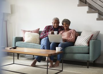 Image of married couple sitting on couch and checking status of tax refund on laptop